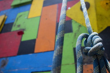 Close-up of a blue climbing knot hanging in front of a colorful gym climbing wall. Low angle shot.