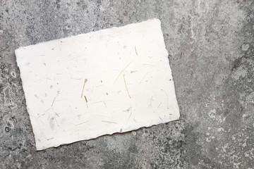 A sheet of handmade cream paper with fragments of plants on the background of a stone table