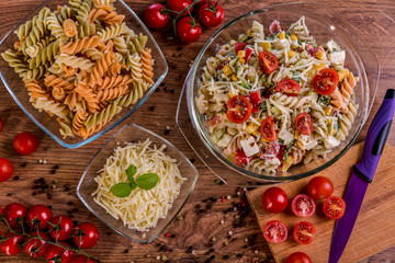 Delicious pasta salad or Mediterranean salad. Tomatoes mozzarella basil corn spice and olive oil on a wooden table. Traditional Italian food
