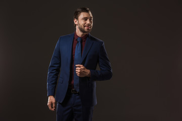 handsome smiling businessman in suit looking away isolated on black