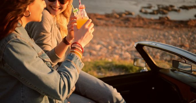 Hipster women in retro convertible car drinking soda at beach