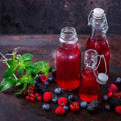 Drink Summer from Mix Berries Decorated with Green Mint. Compote in Glass Bottles. Old dark...
