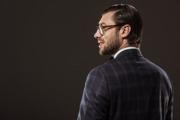 Fototapeta premium back view of handsome smiling man in eyeglasses looking away isolated on black