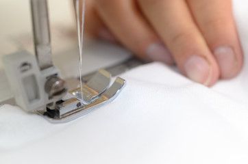 Hands seamstresses with white material behind the sewing machine.