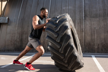muscular african american sportsman exercising with tire on street - Powered by Adobe