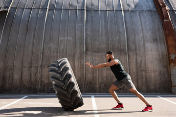 side view of athletic african american man exercising with tire on street