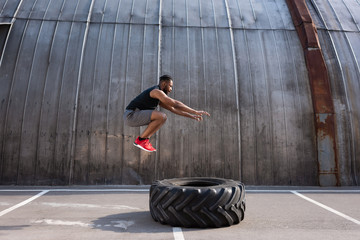 muscular african american sportsman jumping while training with tyre on street