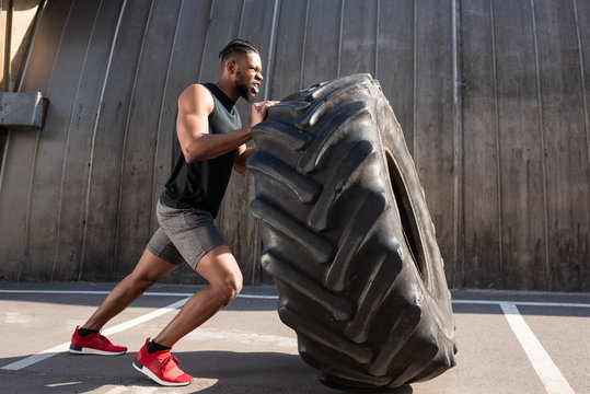 muscular african american sportsman exercising with tire on street