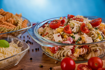 Delicious pasta salad or Mediterranean salad. Tomatoes mozzarella basil corn spice and olive oil on a wooden table. Traditional Italian food