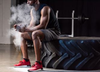 cropped shot of african american sportsman sitting in tyre and applying talcum powder on hands