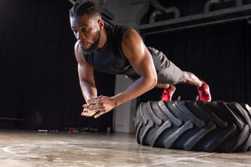 muscular african american sportsman exercising with tyre