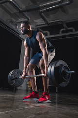 Fototapeta na wymiar low angle view of muscular african american sportsman lifting barbell and looking away in gym