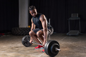 muscular african american sportsman lifting barbell in gym