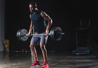 athletic african american man in sportswear lifting barbell and looking away in gym