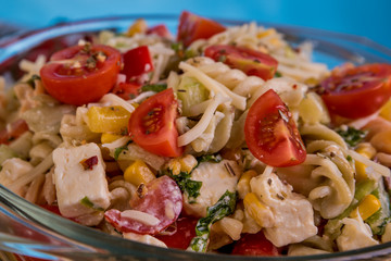 Delicious pasta salad or Mediterranean salad. Tomatoes mozzarella basil corn spice and olive oil on a wooden table. Traditional Italian food