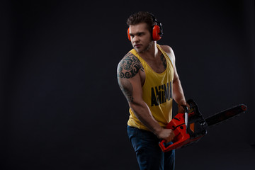 Male construction worker with chainsaw. Portrait of a strong muscular man. Young handsome builder. Male with electric saw. Sexy man with electrical saw. Fashion concept.