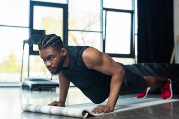 Fototapeta na wymiar muscular african american sportsman doing push ups and looking away in gym