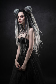 Woman with dreads and black gothic dress posing on dark background