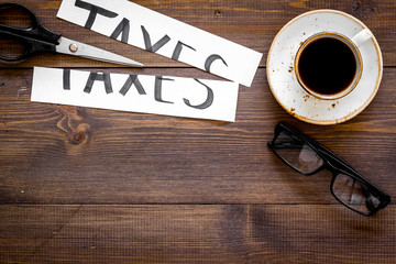 Cut taxes concept. Sciccors cut paper with word Taxes on dark wooden background top view copy space