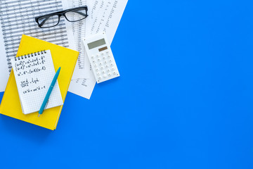 Math homework. Math textbook or tutorial near sheet with numbers, countes, calculator, notebook with formula on blue background top view copy space