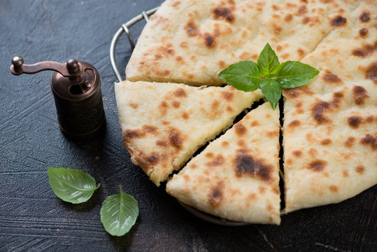 Close-up of sliced ossetian pie with fresh green basil, studio shot, selective focus