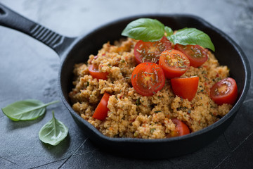 Close-up of a cast-iron frying pan with couscous and cherry tomatoes, studio shot, selective focus