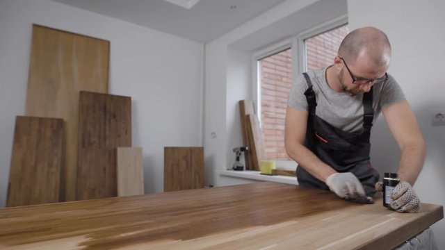 adult man is covering timber boards by varnish in a room of his home, woodworking and furniture assembling
