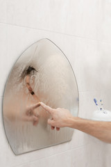 Male hand drawing heart on misted mirror in bathroom