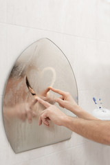 Couple in love drawing heart on misted mirror in bathroom