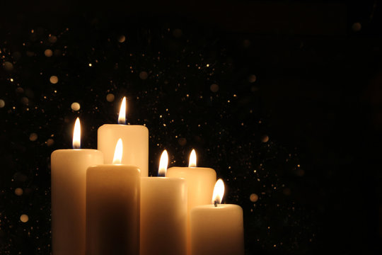 Candles Burning at Night. White Candles Burning in the Dark with lights glow. Focus on six candles in foreground. 
