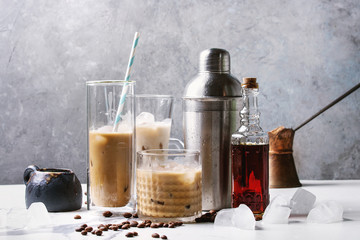 Iced coffee cocktail or frappe with ice cubes and cream in different glasses with jezva, silver...