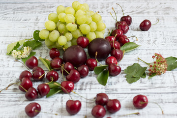 large sweet juicy cherries, plums and grapes, foliage and flowers on a wooden background, healthy eating concept