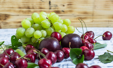 large sweet juicy cherries, plums and grapes, foliage and flowers on a wooden background, healthy eating concept