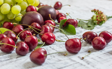 large sweet juicy cherries, plums and grapes, foliage and flowers on a wooden background, healthy eating concept