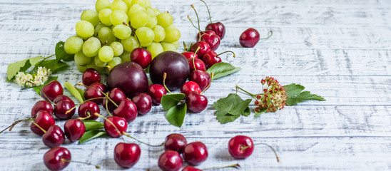 large sweet juicy cherries, plums and grapes, foliage and flowers on a wooden background, healthy eating concept