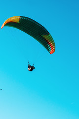 Paraglider flying on colorful parachute in blue clear sky at a bright sunny summer day. Active lifestyle, extreme sport. Adrenaline concept.