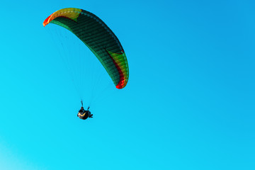 Paraglider flying on colorful parachute in blue clear sky at a bright sunny summer day. Active lifestyle, extreme sport. Adrenaline concept.