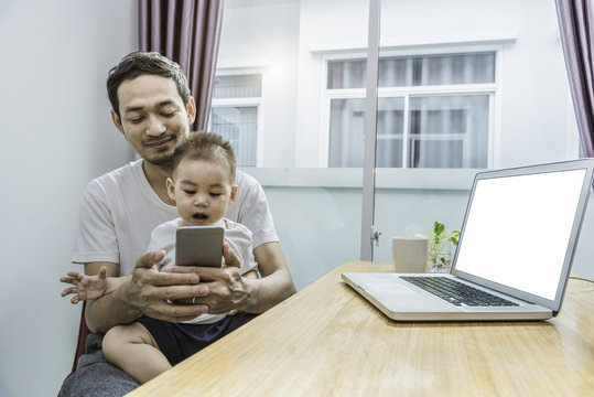 Asian Father And Son Using Smart Phone Together In Home Background. Technology And People Concept. Lifestyles And Happy Family Theme. Internet And Communication Theme. Clipping Path On Laptop Screen.