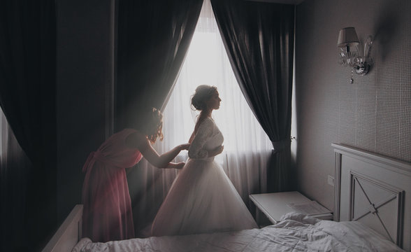 Amazing bride. Young attractive women adjusting a wedding dress on a beautiful bride in the morning.