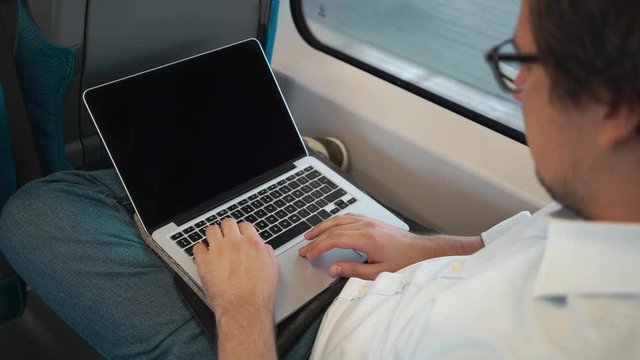 Top view of a young businessman with dark hair using his laptop while riding a train to work. Handheld real time medium shot