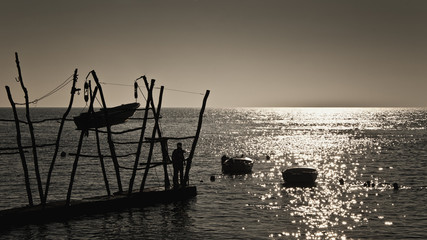 Seascape with boats on the shore and in the sea, silhouette of a man looking reflection on the water, romantic scene