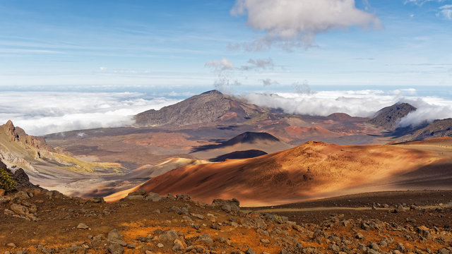 Wide volcanic landscape with lava fields in different colors, wide view, ocher shades, reds, stones in the foreground, cloud shadows, contrast - Location: Hawaii, Island Maui, volcano "Haleakala"