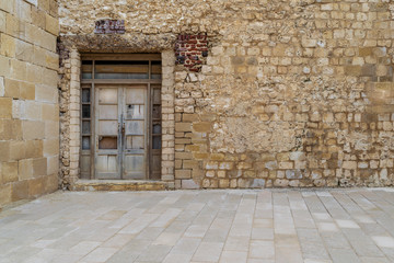 Fototapeta na wymiar Facade of old abandoned stone bricks wall with broken weathered wooden door
