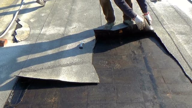 Workers remove the deteriorated bituminous sheath attached to the floor of a building's terrace. Then a new waterproofing layer will be placed.