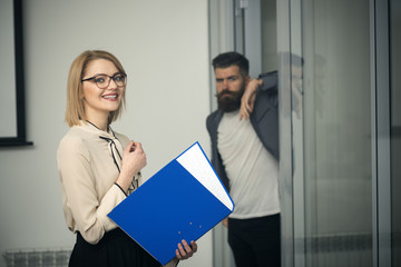 Sexy accountant smile with blurred man on background. Businesswoman in glasses hold binder in office. Happy woman with financial report. Bookkeeping and finance concept. Business and office lifestyle