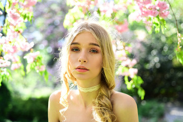 Charming young blond lady with long curled hair in floral garden. Pretty girl with lace strip on her neck enjoying delicate fragrance of blooming flowers, retro style. Tenderness of youth concept