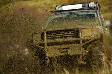 Off road car takes part in racing on nature background. Splash of dirt under SUV on countryside road. Cross country rallying or rally raid Extreme and four wheel drive concept
