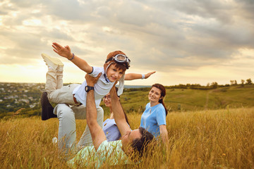 Happy family playing on grass in nature at sunset.