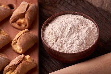 Clay bowl with flour, rolling pin and cottage cheese cookies. baking cookie on dark background. Space for text