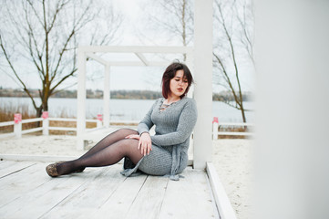 Portrait of brunette girl in gray dress sitting at white wooden construction.